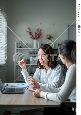 Two women engaged in a productive meeting at a contemporary office, discussing work with laptops and documents. Two women engaged in a productive meeting at a contemporary office, discussing work with laptops and documents. 123362913