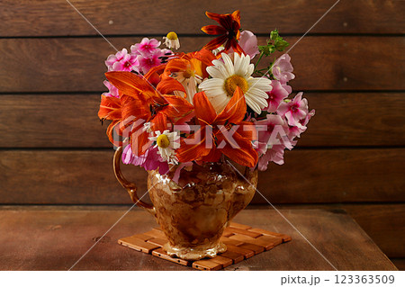 Still life with a bouquet of lilies, chamomile and mallow flowers on an old wooden table, summer and autumn banner, abstract floral arrangement, rustic style, holiday card, selective focus. Still life with a bouquet of lilies, chamomile and mallow flowers on an old wooden table, summer and autumn banner, abstract floral arrangement, rustic style, holiday card, selective focus. 123363509