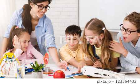 A group of elementary school students are engaged in a STEM learning activity in a classroom setting. They are working with robots and building models, and a teacher is guiding their learning 123364432