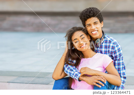 A teen black couple smiles for the camera while sitting on a set of stairs outside. Guy is wearing a plaid shirt and jeans, while the girl is wearing a pink shirt and jeans. A teen black couple smiles for the camera while sitting on a set of stairs outside. Guy is wearing a plaid shirt and jeans, while the girl is wearing a pink shirt and jeans. 123364471