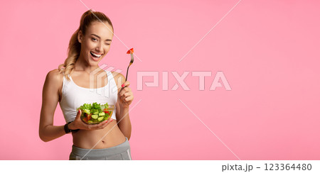 Healthy Diet. Sporty Girl Eating Fresh Salad Winking At Camera Over Yellow Studio Background. Copy Space 123364480