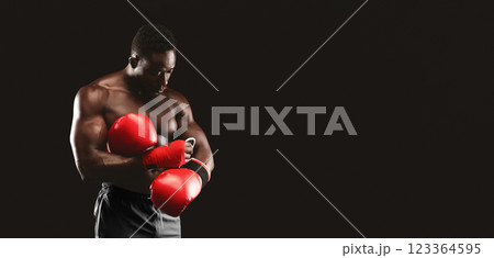 A muscular boxer wearing red boxing gloves prepares for a fight against a black background. A muscular boxer wearing red boxing gloves prepares for a fight against a black background. 123364595