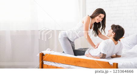 Cheerful young woman cuddling with her man in bed. Loving couple have fun at home, hugging and smiling, copy space 123364666