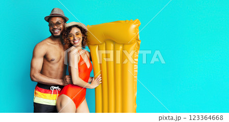 Black couple stand together against a bright blue background. The man is wearing sunglasses and a hat, and the woman is wearing a swimsuit, hat, and sunglasses, copy space Black couple stand together against a bright blue background. The man is wearing sunglasses and a hat, and the woman is wearing a swimsuit, hat, and sunglasses, copy space 123364668