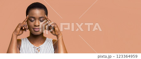 African American young woman meditating with her eyes closed. She is touching her temples with her index fingers, indicating relaxation and focus 123364959