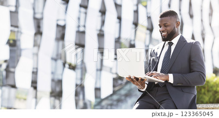 Smiling Black Business Guy Using Laptop Computer Browsing Internet During Coffee Break In Urban City Area. Empty Space 123365045