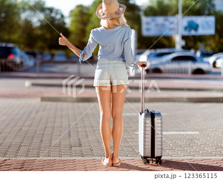 Arriving Home Concept. Tourist trying to catch taxi, standing with suitcase and showing thumbs up, copyspace, back view 123365115