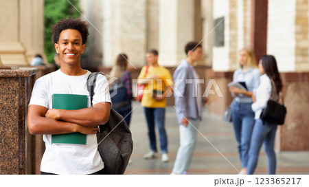 Enjoying university life. African guy holding books and smiling, standing against friends 123365217