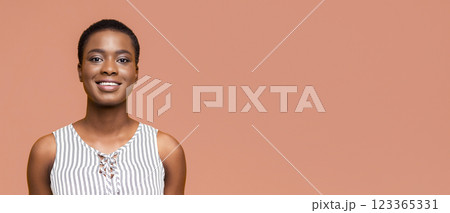 A close-up portrait of a smiling Black woman with short hair wearing a white and black striped top against a peach-colored background, panorama with copy space A close-up portrait of a smiling Black woman with short hair wearing a white and black striped top against a peach-colored background, panorama with copy space 123365331