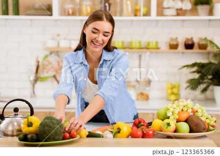 A woman smiles as she arranges fresh produce on a plate in her kitchen. A woman smiles as she arranges fresh produce on a plate in her kitchen. 123365366