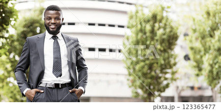 Portrait of handsome confident black man in suit with his hands in pockets against modern office center background, copy space 123365477