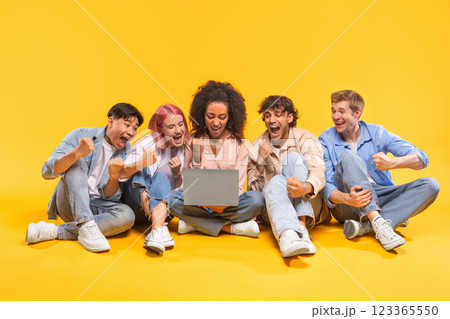 A group of five diverse friends are sitting on a yellow background, looking at a laptop and celebrating. They are all smiling and have their hands in the air. A group of five diverse friends are sitting on a yellow background, looking at a laptop and celebrating. They are all smiling and have their hands in the air. 123365550