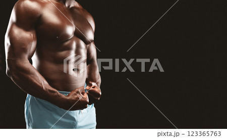 A muscular man with defined abs poses against a black background, flexing his bicep. A muscular man with defined abs poses against a black background, flexing his bicep. 123365763
