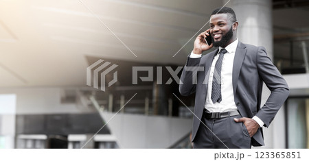 Young attractive african businessman making phone call, standing near office building with his hand in pocket Young attractive african businessman making phone call, standing near office building with his hand in pocket 123365851