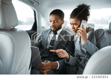African American man and woman in business attire are working in a car. They are both focused on their work, which suggests they are serious and dedicated to their business. African American man and woman in business attire are working in a car. They are both focused on their work, which suggests they are serious and dedicated to their business. 123365853