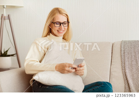 A woman sits on a couch, smiling, and using a smartphone. A woman sits on a couch, smiling, and using a smartphone. 123365963