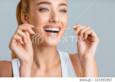 This image shows a woman flossing her teeth with a bright smile. Her bright white teeth and healthy smile are a great example of the importance of proper dental hygiene. 123365967