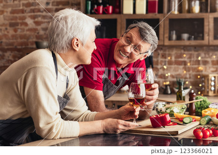 Romantic senior couple drinking wine and preparing healthy meal together in kitchen, chatting, empty space 123366021