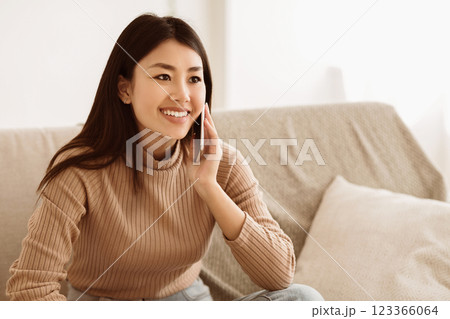 Asian Girl Talking on Mobile Phone and Smiling, Sitting on Couch at Home, Free space Asian Girl Talking on Mobile Phone and Smiling, Sitting on Couch at Home, Free space 123366064