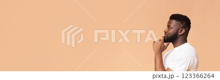 This image features a young African American man thinking while looking to the side. He is wearing a white t-shirt and standing against a peach-colored background, copy space This image features a young African American man thinking while looking to the side. He is wearing a white t-shirt and standing against a peach-colored background, copy space 123366264