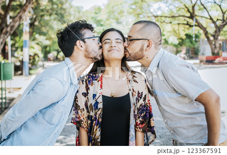 Love triangle concept. Polygamy concept. Two men kissing a girl cheek. Portrait of two guys kissing a girl cheek. Two young men kissing a woman cheek outdoor 123367591