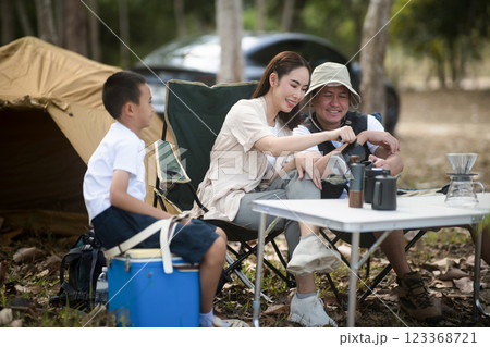 The family are enjoying their time while camping in the forest. The mother is pouring a drink for the father. 123368721