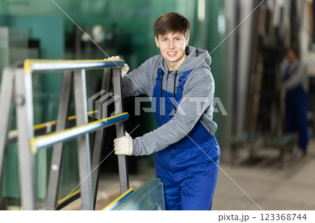 Guy glazer employee in blue overall works in glass processing shop Guy glazer employee in blue overall works in glass processing shop 123368744