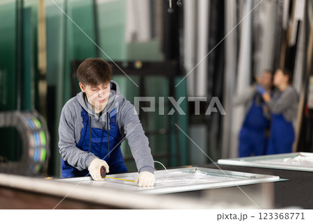 Young guy measuring sheet of glass in factory 123368771