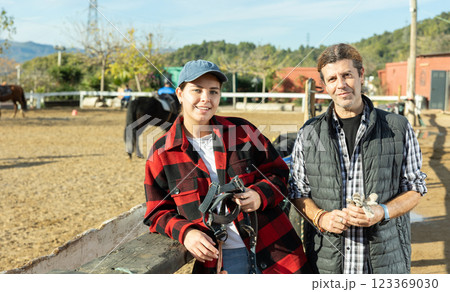 Portrait of two male female grooms posing on yard of horse riding club Portrait of two male female grooms posing on yard of horse riding club 123369030