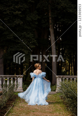 Romantic Woman in a Light Blue Gown Posing on a stone balustrade in a picturesque garden. 123369053