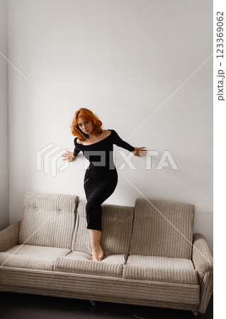 Elegant woman in black dress on sofa against white wall Elegant woman in black dress on sofa against white wall 123369062