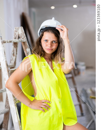 Sexy young woman in a yellow vest and protective helmet poses playfully in renovated room 123369180