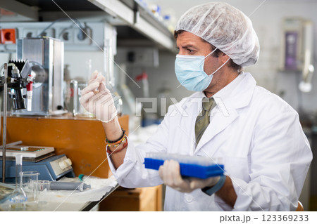Middle-aged Latin male scientist researcher holding tripod and looking at reaction in test tube while performing biochemical tests in lab Middle-aged Latin male scientist researcher holding tripod and looking at reaction in test tube while performing biochemical tests in lab 123369233