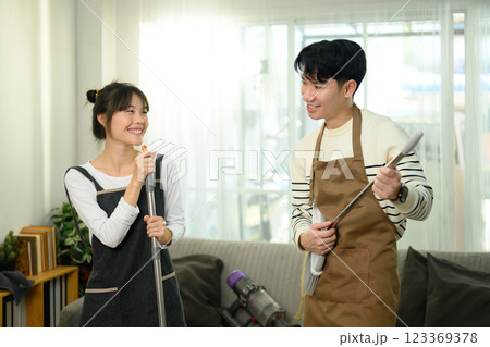 Playful couple wearing aprons cleaning their home. Chores and home care concept Playful couple wearing aprons cleaning their home. Chores and home care concept 123369378