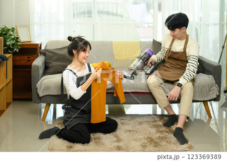 Happy young couple wearing aprons folding laundry and tidying up their living room 123369389