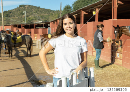 Portrait of young female stable visitor smiling at camera in horse club on sunny spring day Portrait of young female stable visitor smiling at camera in horse club on sunny spring day 123369396