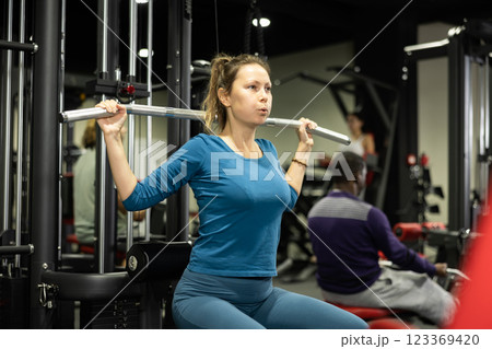 Caucasian woman doing reps on lat pull down machine in gym 123369420