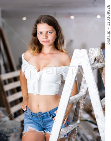 Sexy young woman in a white blouse and short shorts poses playfully in renovated room Sexy young woman in a white blouse and short shorts poses playfully in renovated room 123369526