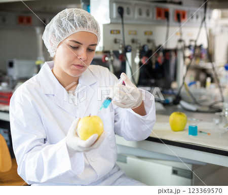 Young woman chemist makes an injection to a yellow apple Young woman chemist makes an injection to a yellow apple 123369570