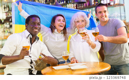 Happy international sport fans waving Ukrainian flag while watching football game and drinking beer in the pub Happy international sport fans waving Ukrainian flag while watching football game and drinking beer in the pub 123369748