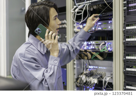 テレビ局の副調整室の機材の前でスマホを手に作業をする若い男性　撮影協力:スカパー東京メディアセンター 123370481