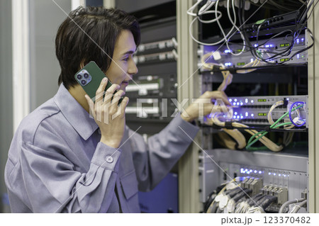 テレビ局の副調整室の機材の前でスマホを手に作業をする若い男性 撮影協力:スカパー東京メディアセンター テレビ局の副調整室の機材の前でスマホを手に作業をする若い男性 撮影協力:スカパー東京メディアセンター 123370482