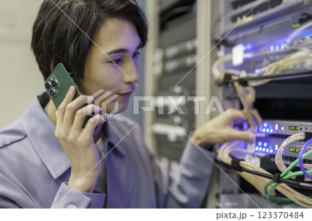 テレビ局の副調整室の機材の前でスマホを手に作業をする若い男性　撮影協力:スカパー東京メディアセンター 123370484