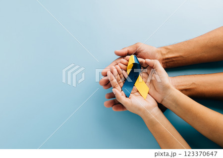 Down Syndrome awareness, hands hold a ribbon on blue background. Highlighting Down Syndrome Day 123370647