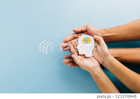 Hands holding a brain jigsaw in a head paper cut symbolize Down Syndrome awareness. 123370648