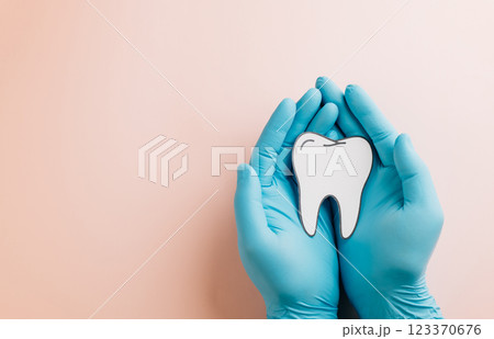 Dentist Day. Gloved doctor hands hold a tooth paper cutout on pink background. 123370676