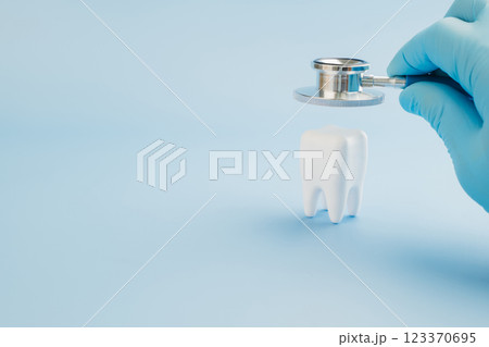 Dentist Day features a doctor using a stethoscope on a tooth model against blue 123370695