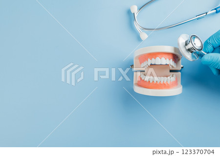Dentist Day, a gloved doctor examines a dental model with a stethoscope. Recognizing dentists Dentist Day, a gloved doctor examines a dental model with a stethoscope. Recognizing dentists 123370704