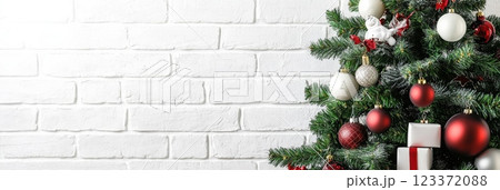 Close-up of a Christmas tree with red and white ornaments, set against a white brick wall. Holiday mockup background. 123372088