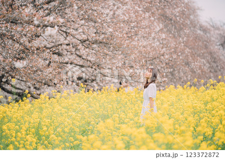 桜並木を背景に菜の花畑を歩く女性 桜並木を背景に菜の花畑を歩く女性 123372872